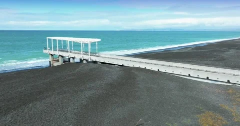 A pier extends over a black sand beach in Marine Parade, Napier, New Zealand Video stock 333168570