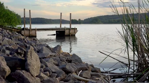 Pier on a forest lake at sunset. Large stones by the lake Evening sky over water Stock Footage 155618745