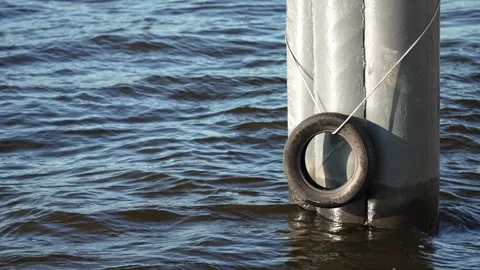 Pier mooring pole and bumper tire in calm rippling water Stock Footage 346048884