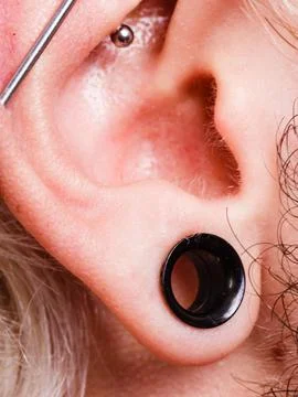 Pierced man ear, black plug tunnel, industrial and rook Stock Photos