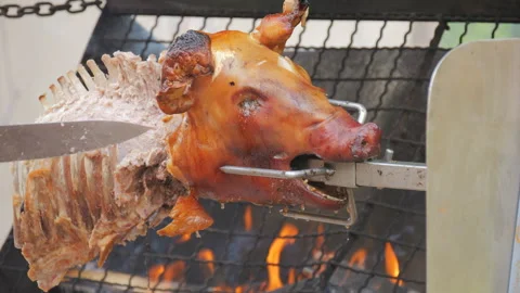 Pig carcass on a spit. The chef cuts pieces of meat with a knife in slow motion Stock Footage 249957363