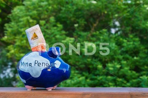 A Piggy Bank On A Plank In Front Of A Green Tree