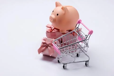 Piggy bank on stack of gift boxes, shopping cart. White background Stock Photos