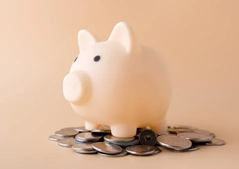 Piggy bank stands on coins on a beige background Stock Photos