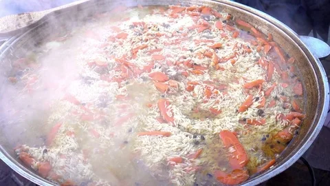 Pilaf is cooked on the grill in a large cauldron. Boiling liquid and steam Stock Footage 84551595