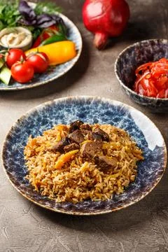 Pilaf with lamb meat in large dish, plate of tomato salad and dish with veget Stock Photos