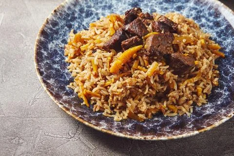 Pilaf with lamb meat in large dish, plate of tomato salad and dish with veg.. Stock Photos