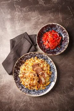 Pilaf with lamb meat in large dish and plate of tomato salad Stock Photos