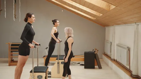 Pilates lesson on chair, side view of blond elderly personal trainer coaching Stock Footage 229437311