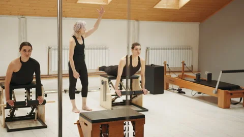 Pilates lesson on chair, side view of blond elderly personal trainer coaching Stock Footage 229438101