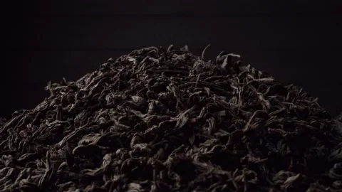 A pile of black loose-leaf tea slowly rotates on a dark black background. Close Stock Footage 237875003