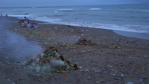 A pile of burning offerings on the beach in front of praying Balinese family Stock Footage 74289503
