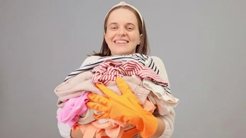 Pile of clean laundry. Laundry stack at home. Pleased woman wearing hair band Stock Footage 257762697