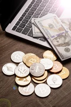 Pile of cryptocurrency coins and stack of dollars on the table near the laptop Stock Photos
