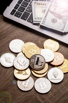 Pile of cryptocurrency coins and stack of dollars on the table near the laptop Stock Photos