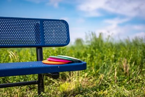 Pile of discs resting on a bench in the golf course park Stock Photos
