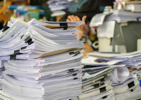 Pile of documents on desk stack up high waiting to be managed. Stock Photos