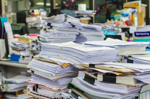 Pile of documents on desk stack up high waiting to be managed. Stock Photos