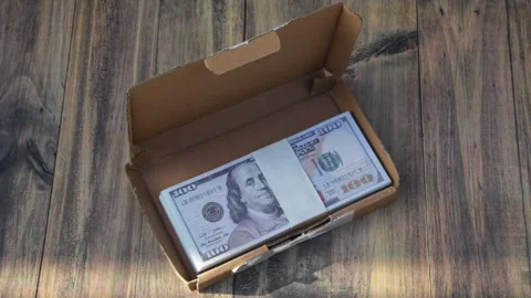 A pile of dollar bills in a small cardboard container on a wooden table Stock Footage 319795616