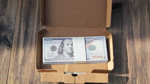 A pile of dollar bills in a small cardboard container on a wooden table Stock Footage 319795622