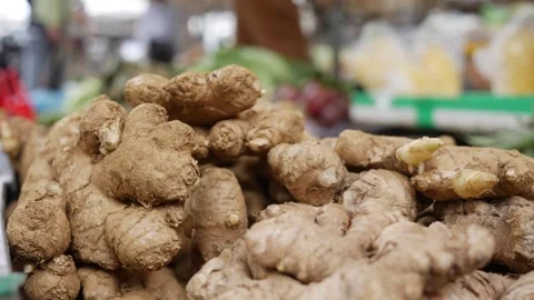 Pile of dried ginger roots sits on a market stall, with other goods and people Stock Footage 328097130