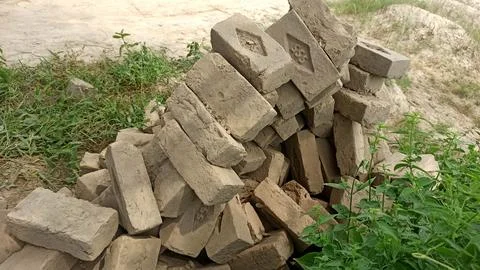 Pile Of Handmade Construction Bricks On Ground With Green Weeds Stock Photos