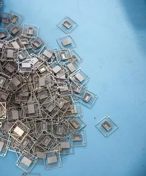 Pile of Metallic Semiconductor Lead Frames on Blue Table Surface Фото