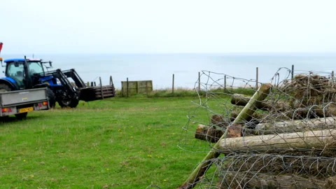 Pile of old rotten fence posts and tractor on the seaside hill edge Vídeos de archivo 249456777