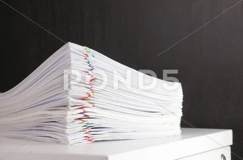 Pile overload paperwork on white cabinet with black wall Stock Photos