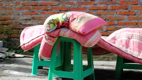 A pile of pillows on a plastic chair drying in the sun Stock Footage 320328146
