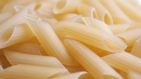 A pile of raw yellow pipe-shaped pasta lies on the surface. Raw pasta feathers Video stock 221796176