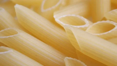 A pile of raw yellow pipe-shaped pasta lies on the surface. Raw pasta feathers Video stock 221828575