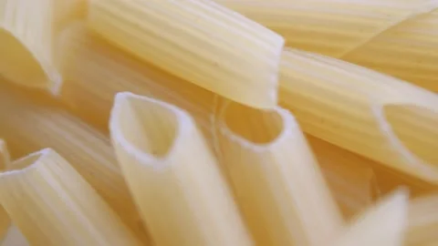 A pile of raw yellow pipe-shaped pasta lies on the surface. Raw pasta feathers Video stock 222631411