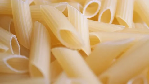 A pile of raw yellow pipe-shaped pasta lies on the surface. Raw pasta feathers Video stock 222795443