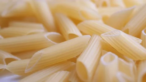 A pile of raw yellow pipe-shaped pasta lies on the surface. Raw pasta feathers Video stock 222974722