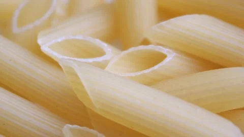 A pile of raw yellow pipe-shaped pasta lies on the surface. Raw pasta feathers Video stock 223162737
