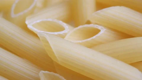 A pile of raw yellow pipe-shaped pasta lies on the surface. Raw pasta feathers Video stock 223327150