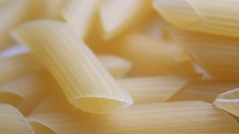 A pile of raw yellow pipe-shaped pasta lies on the surface. Raw pasta feathers Video stock 223515344