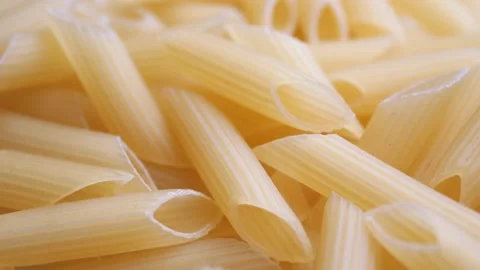 A pile of raw yellow pipe-shaped pasta lies on the surface. Raw pasta feathers Video stock 223776369