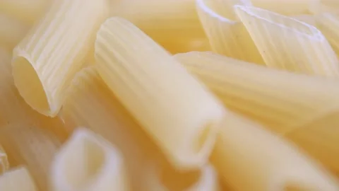 A pile of raw yellow pipe-shaped pasta lies on the surface. Raw pasta feathers Stock Footage 225333483