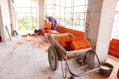 Pile of red blocks in wheelbarrow, worker builds wall with bricks and morta.. Stock Photos