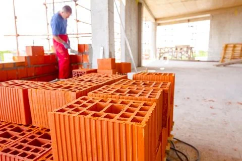 Pile of red blocks, worker builds wall with bricks and mortar, building site Fotos de archivo