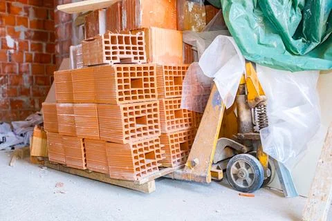 Pile of red bricks on pallet jack in storage room of building siteStacked r.. Foto stock