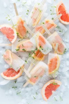 A pile of refreshing icy cold grapefruit thyme popsicles on ice cubes. Stock Photos