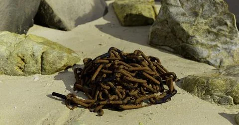 Pile of rusty chains resting on sandy ground surrounded by stones Stock Illustration