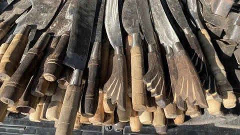 A pile of sharp tools such as knives, machetes, axes, sickles, metal sickles Stock Photos