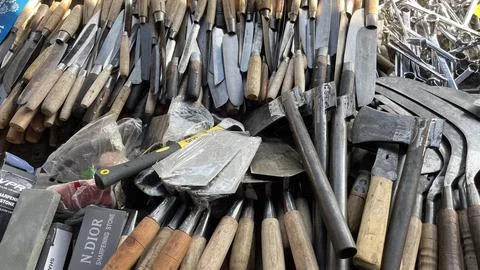 A pile of sharp tools such as knives, machetes, axes, sickles, metal sickles Stock Photos