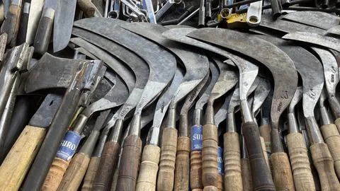A pile of sharp tools such as knives, machetes, axes, sickles, metal sickles Stock Photos