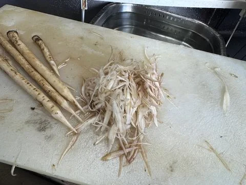 Pile of shaved burdock root gobo strips and whole roots on cutting board, Japan Stock Photos