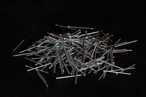 A pile of small wood nails on a black background, showcasing their metallic.. Stock Photos